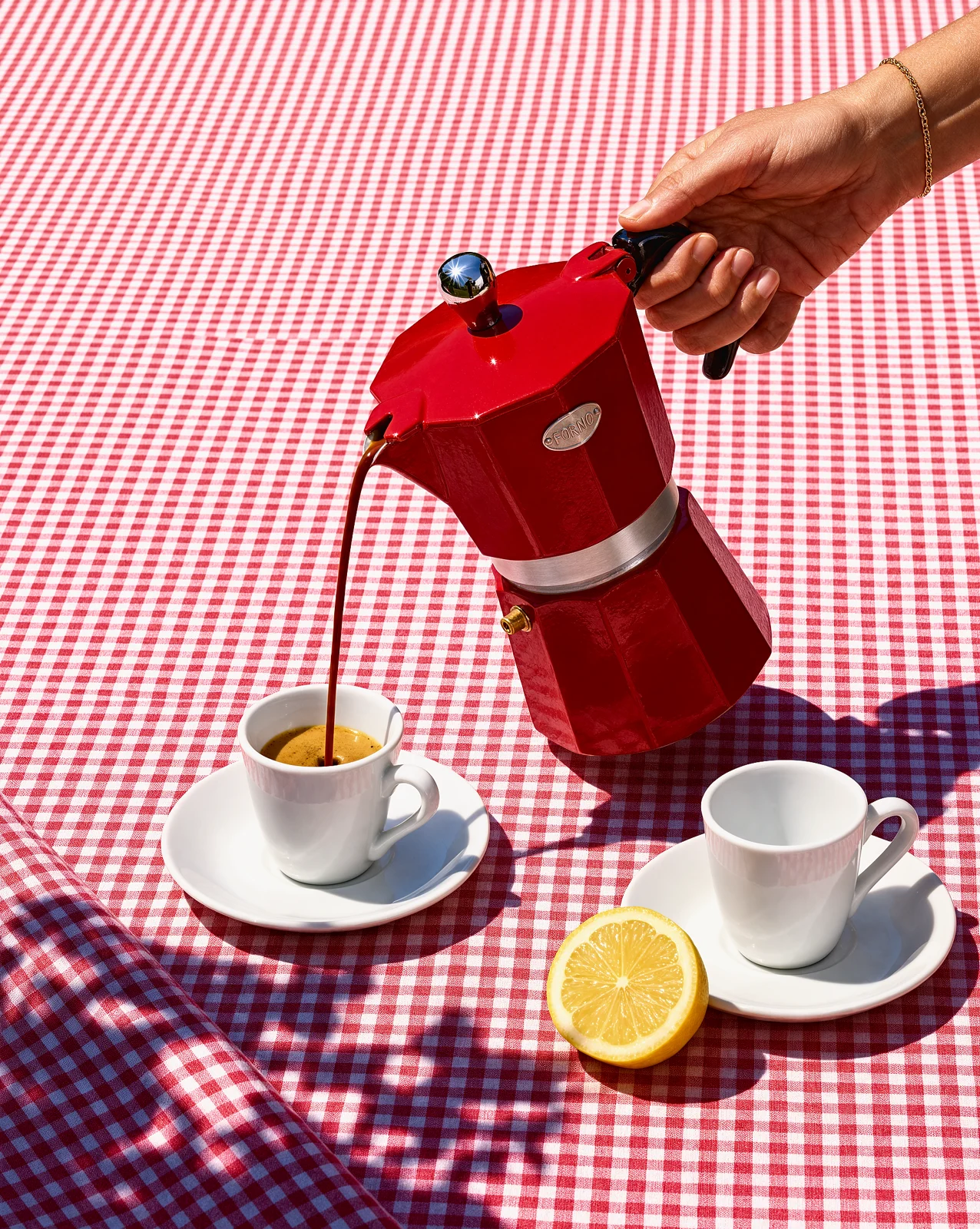 The same moka pot pouring espresso on a red gingham tablecloth