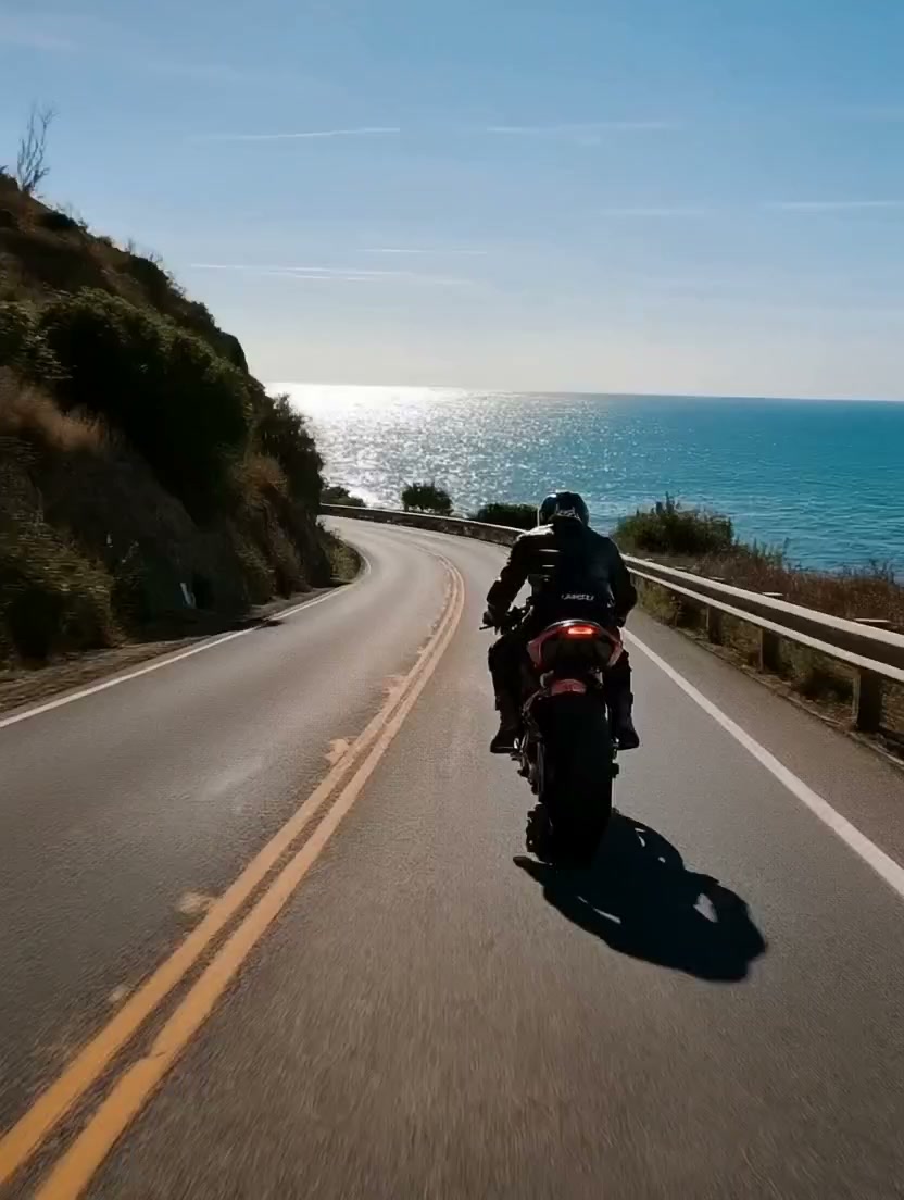 Motorcyclist riding along a sunlit coastal road.