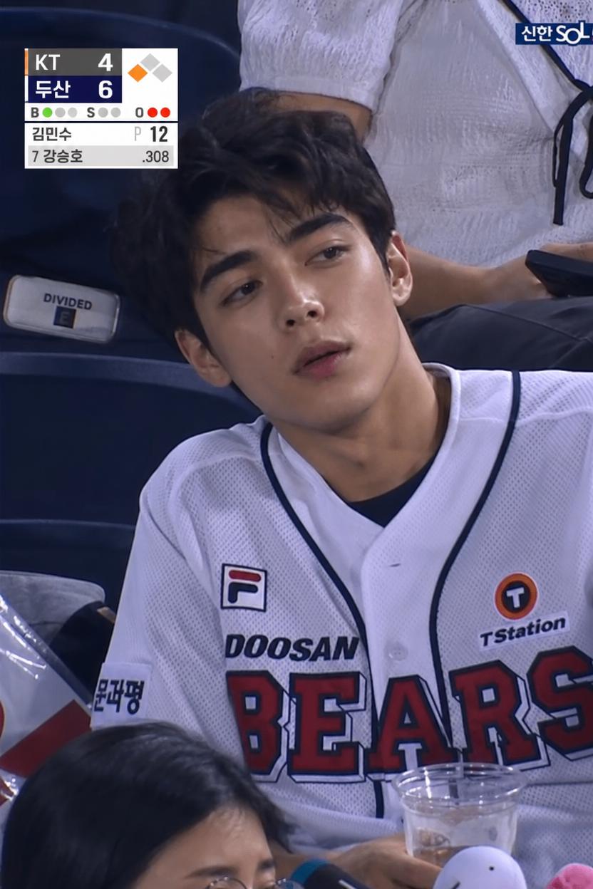 A Man Wearing A Doosan Bears Jersey Is Seated At A Baseball Game Holding A Drink
