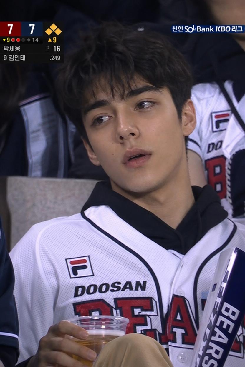 A Man Wearing A Doosan Bears Jersey Enjoys A Baseball Game While Holding A Drink In The Stadium