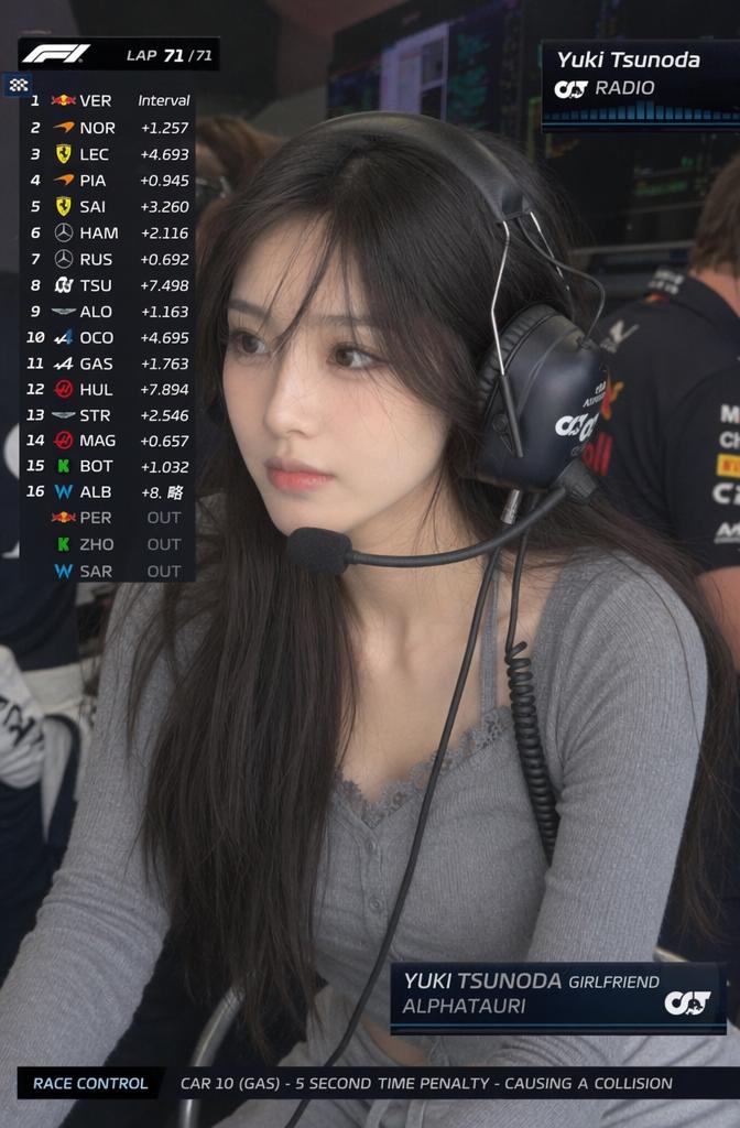 A Woman Wearing A Headset Is Seated In A Formula 1 Team Environment With Race Standings Displayed On-Screen