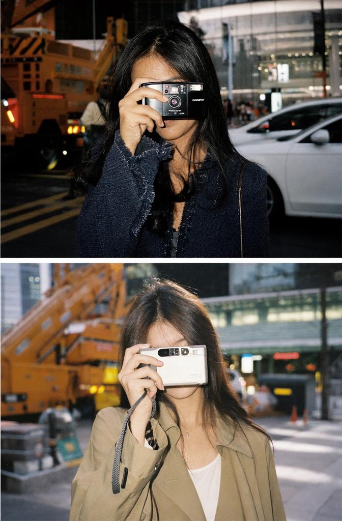 A Woman Is Photographed Covering Her Face With A Phone In A Busy Urban Street Setting Featuring Cars And Construction Equipment