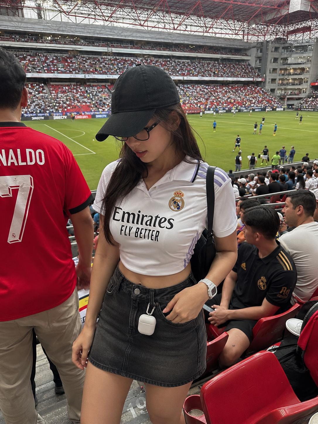 A Woman Wearing A Real Madrid Jersey And A Black Skirt Stands In A Stadium During A Soccer Match