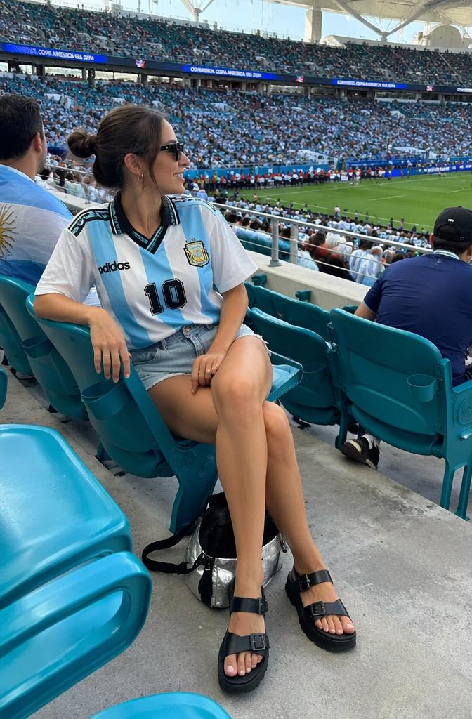 Casual stadium-chic aesthetic featuring a relaxed young woman in a vintage Argentina socc...