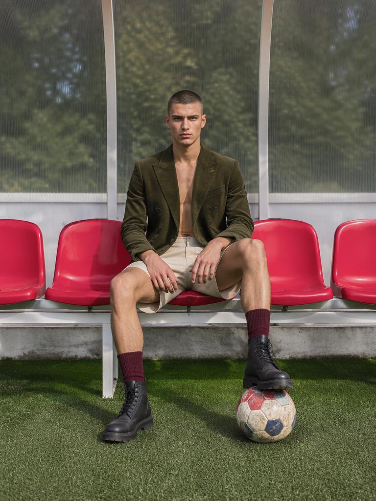 The stark juxtaposition of a high-fashion editorial male subject sitting on a vibrant red...