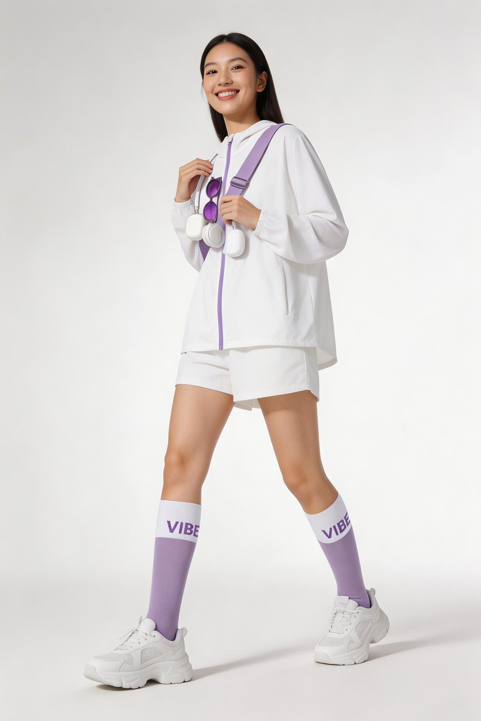A Woman Dressed In A Sporty White And Purple Outfit Poses Confidently In A Minimalist Studio Setting