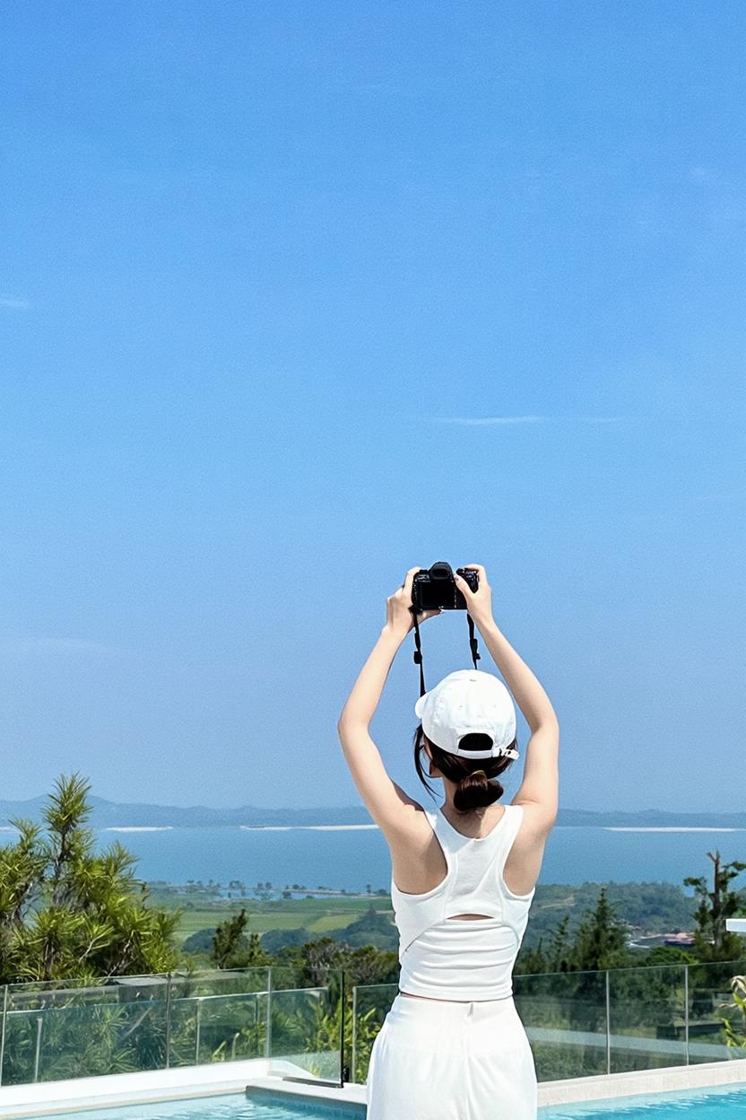 A Woman Stands By A Pool Capturing The Scenic View Of The Ocean And Greenery With Her Camera On A Clear Sunny Day